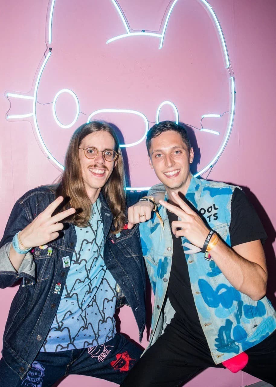 Two people posing in front of a neon Cool Cats sign.